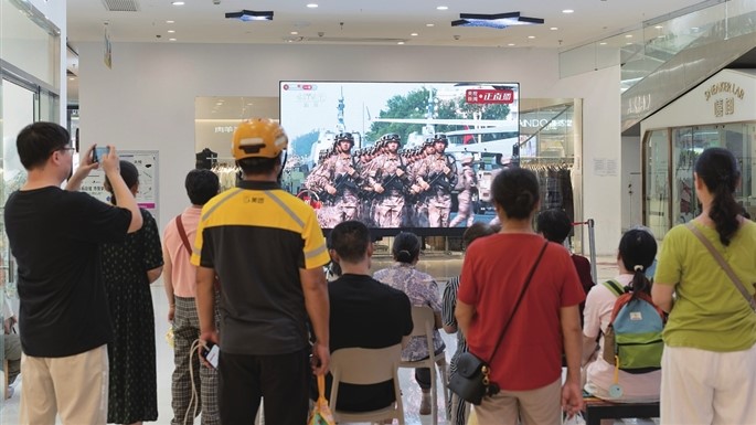 顾客在商场内观看纪念大会现场直播